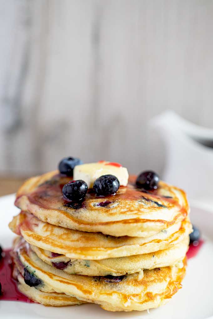 Supper Fluffy Pancakes with blueberries stacked up high and drizzled with blueberry syrup and topped with butter. 