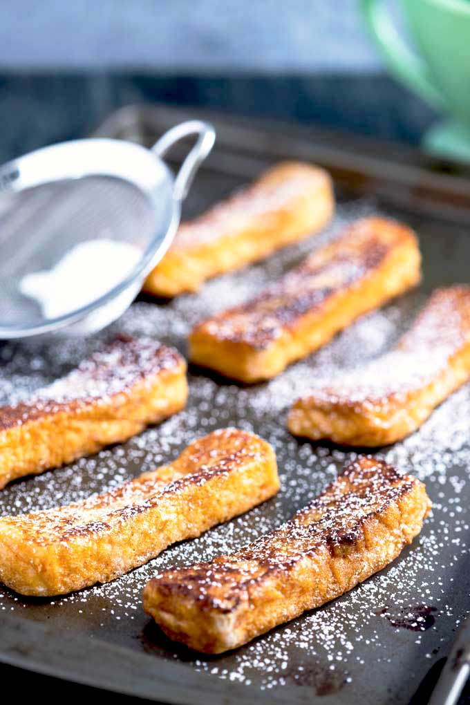 Homemade Cinnamon sticks on a sheet pan getting dusted with powdered sugar