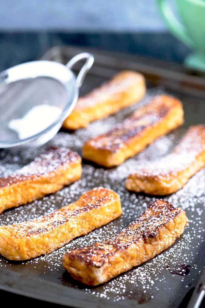 Homemade Cinnamon sticks on a sheet pan getting dusted with powdered sugar