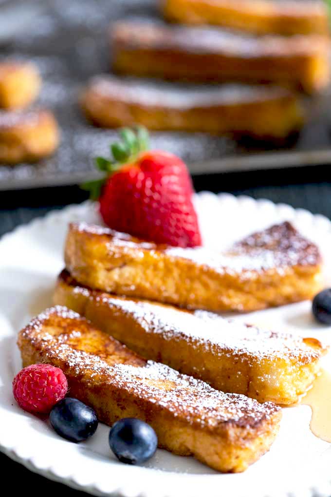 Cinnamon French Toast Sticks served on a white plate with berries and maple syrup.