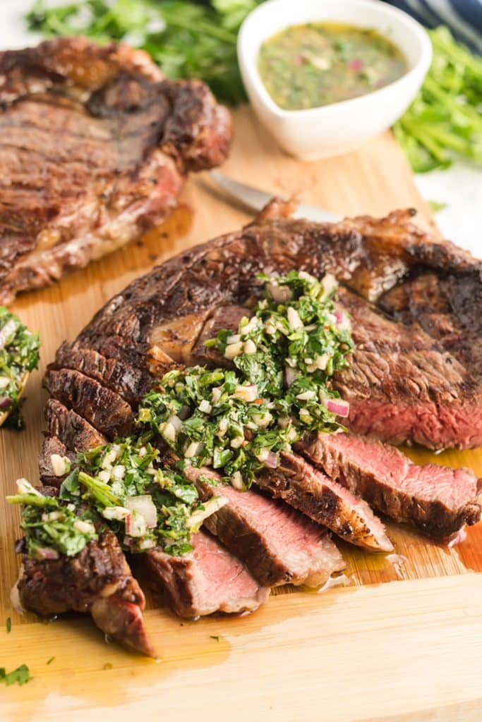 Grilled Steak sliced and topped with chimichurri sauce on a cutting board.