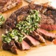 Grilled Steak sliced and topped with chimichurri sauce on a cutting board.