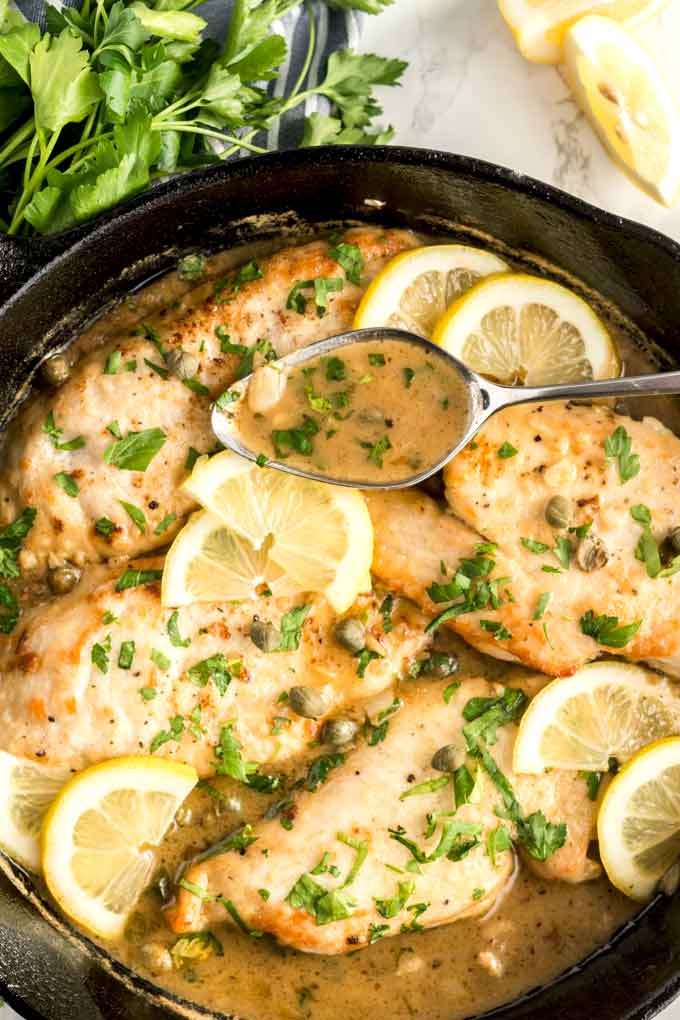 Chicken Picatta in a skillet garnished with lemon slices and chopped parsley.