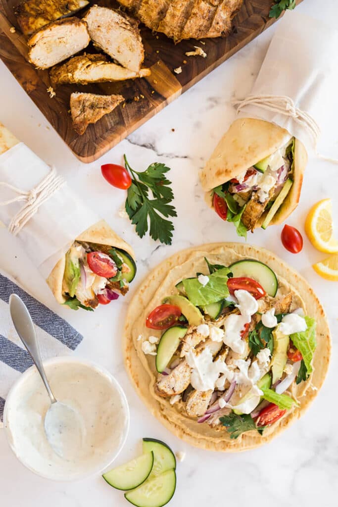 Making shawarma wraps, pita bread is topped with hummus, slices of shawarma chicken, cucumbers, lettuce, onions and avocados and topped with a creamy sauce