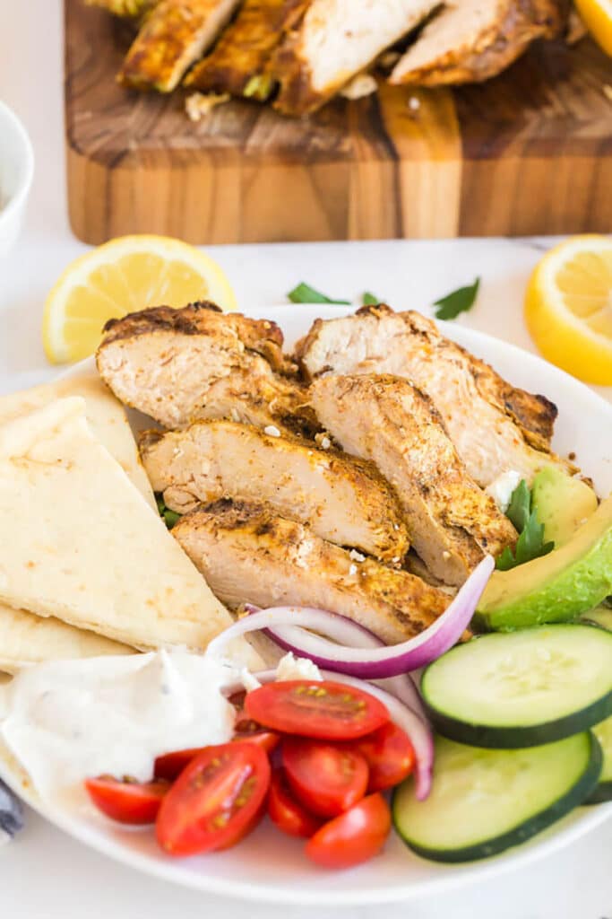 Chicken Shawarma on a plate with avocado slices, cucumbers, tomatoes, onions, creamy garlic sauce and pita bread.