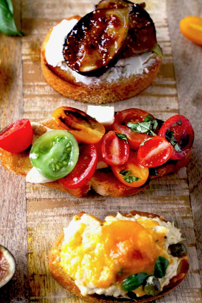 Three types of crostini appetizers served on a wooden block