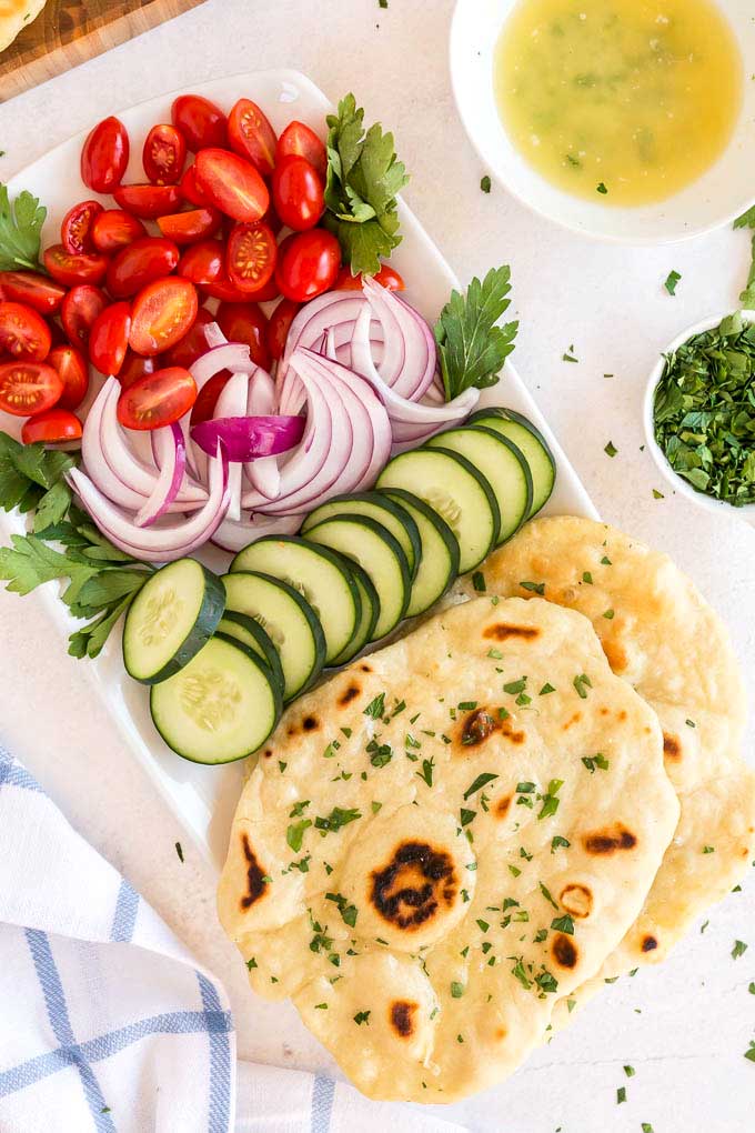 a white rectangular plate with cherry tomatoes, onion and cucumber slices and flatbread