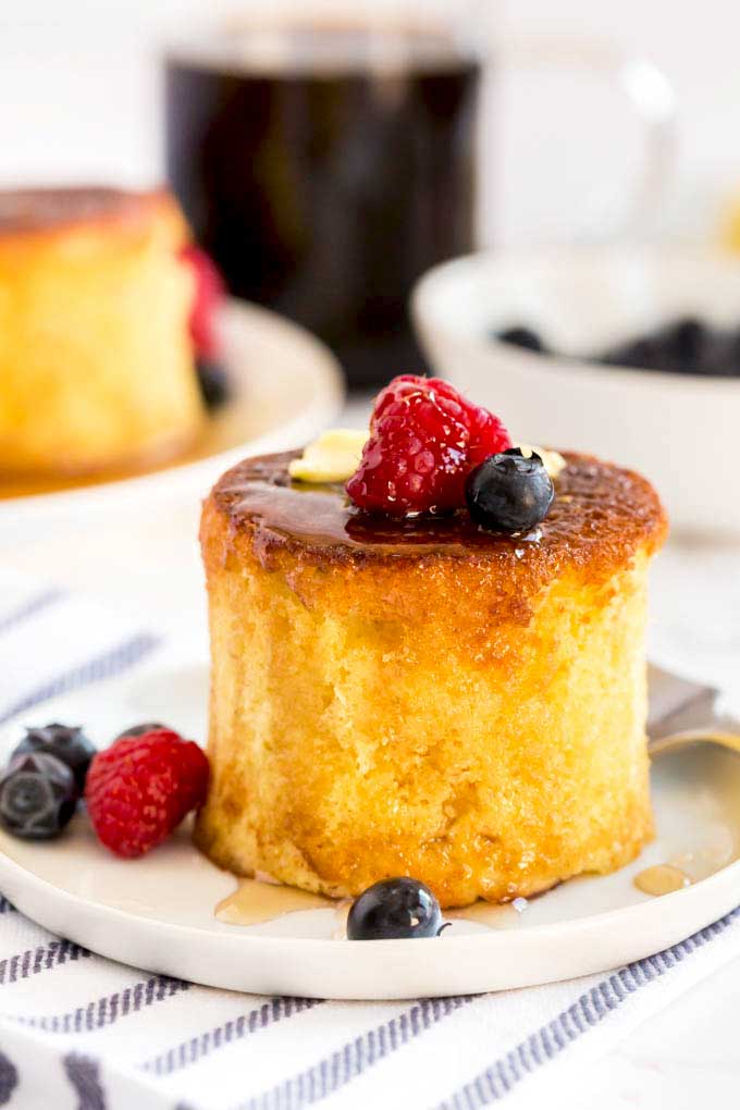 A tall and fluffy Japanese Souffle pancake drizzled with syrup, topped with a pat of butter and berries on a white plate.
