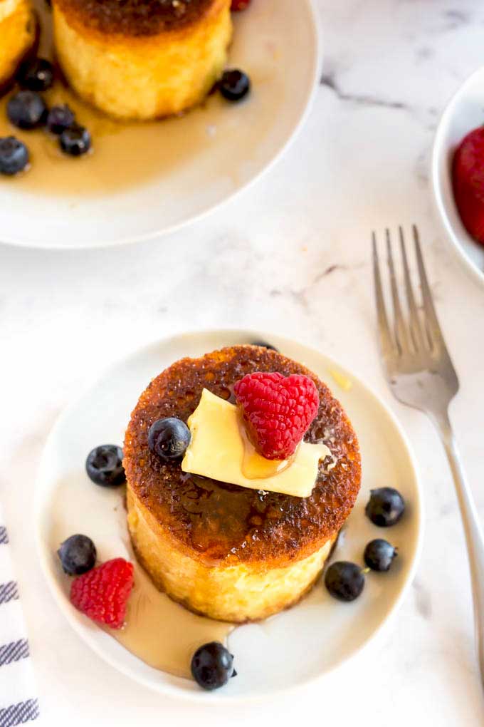 Top view of a fluffy souffle pancake served with berries, butter and  drizzled with syrup. 