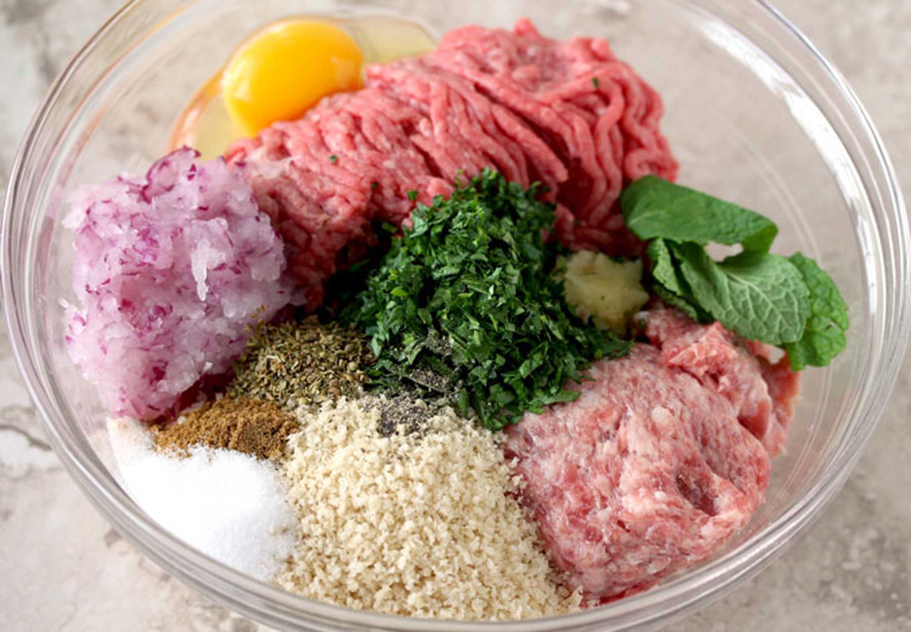 Ground beef, pork, herbs, onion and other ingredients fin a large bowl