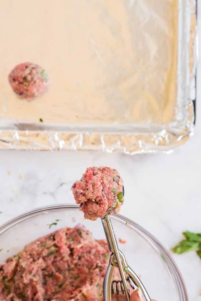 Scooping meat mixture with a scooper to shape the meatballs