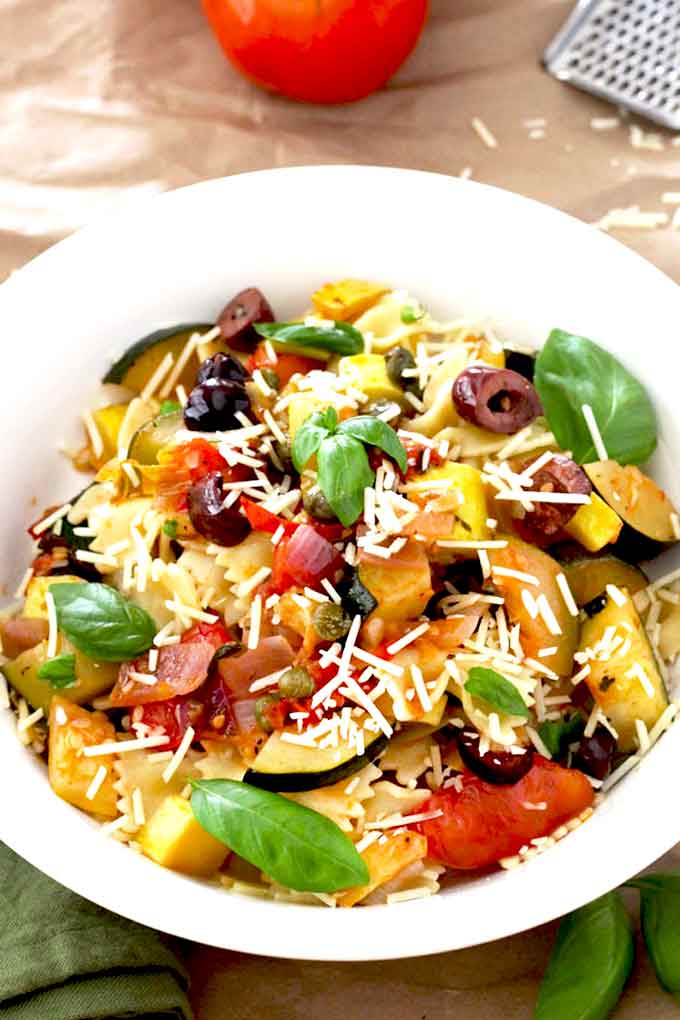 A white bowl filled with veggie pasta and top with Parmesan cheese.