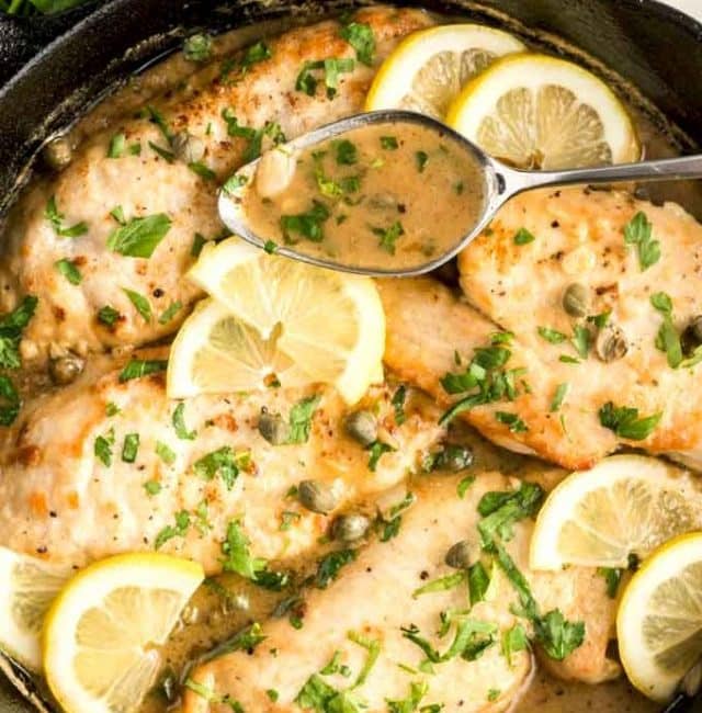 Chicken Picatta in a skillet garnished with lemon slices and chopped parsley.