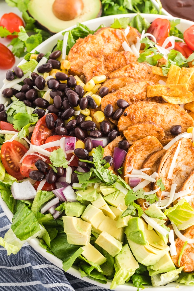 Close up view of barbecue salad with black beans, BBQ chicken, onions, avocados, corn, tomatoes and shredded cheese.