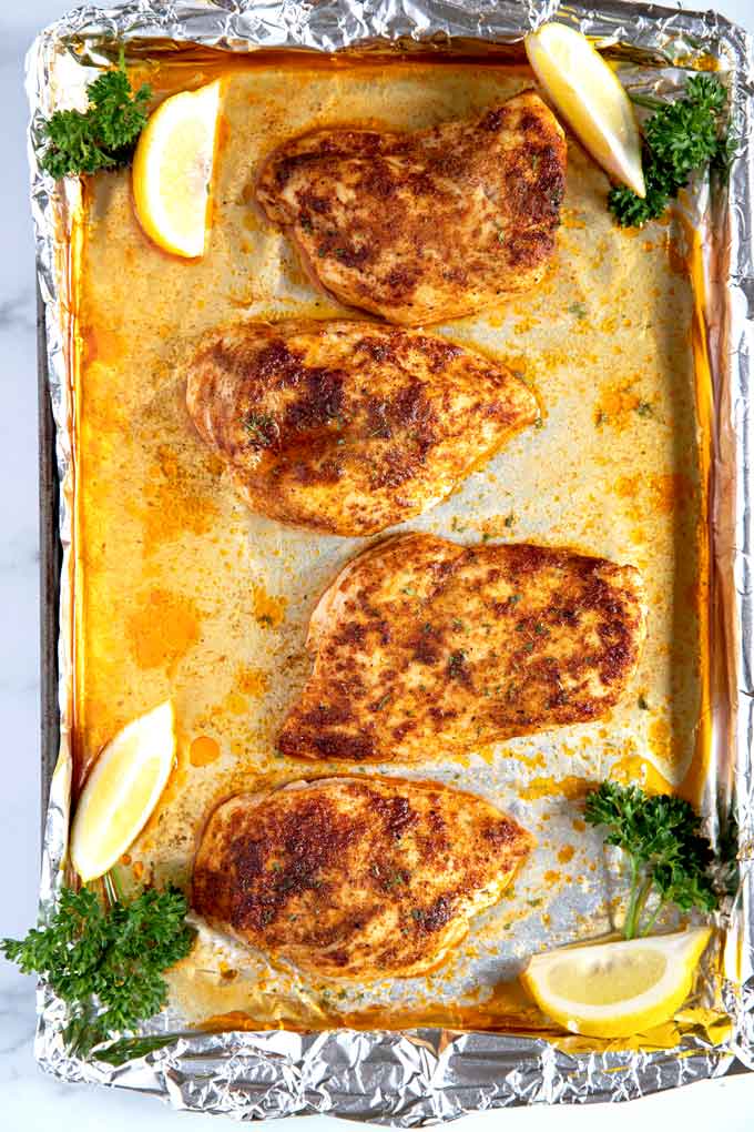 Boneless skinless chicken breasts seasoned on a baking sheet pan.