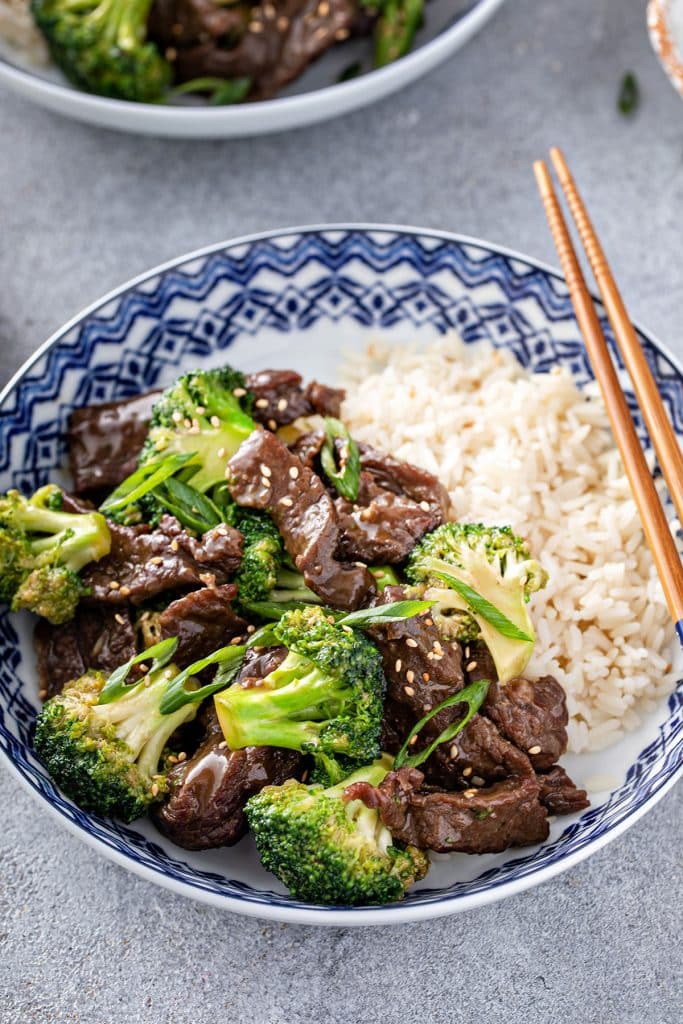 a bowl with beef and broccoli, garnished with sesame seeds, chopped green onion and white rice