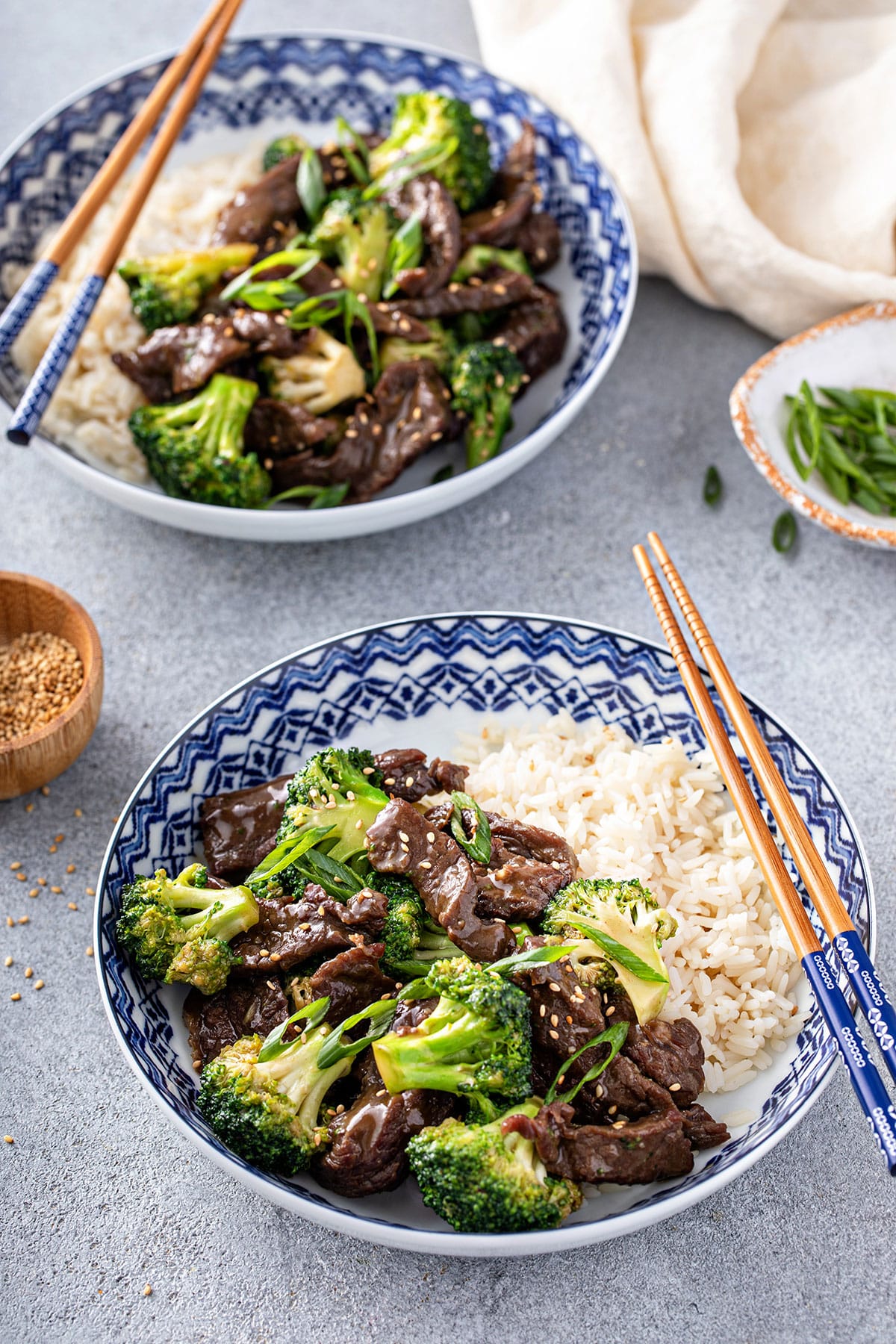 Chopsticks starting to lift broccoli beef from a white bowl.