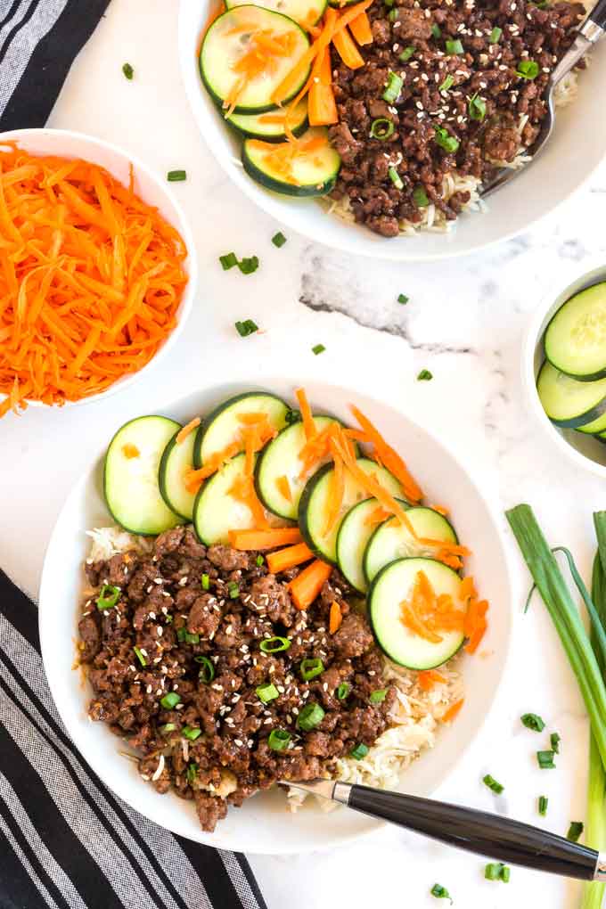 Two bowls of Korean Beef over rice with pickled veggies on a white surface.