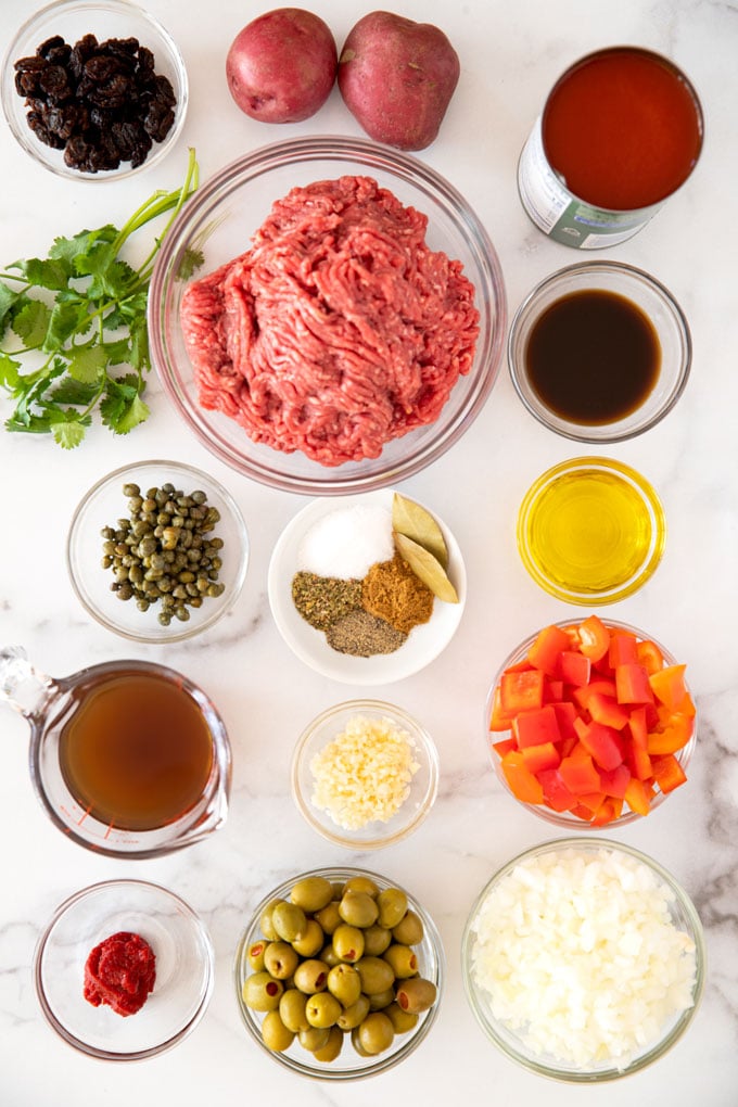 Ingredients to make beef picadillo set in bowls on a marble counter.