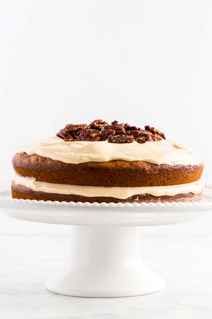 Two layered pumpkin cake with cream cheese frosting on a cake pedestal.