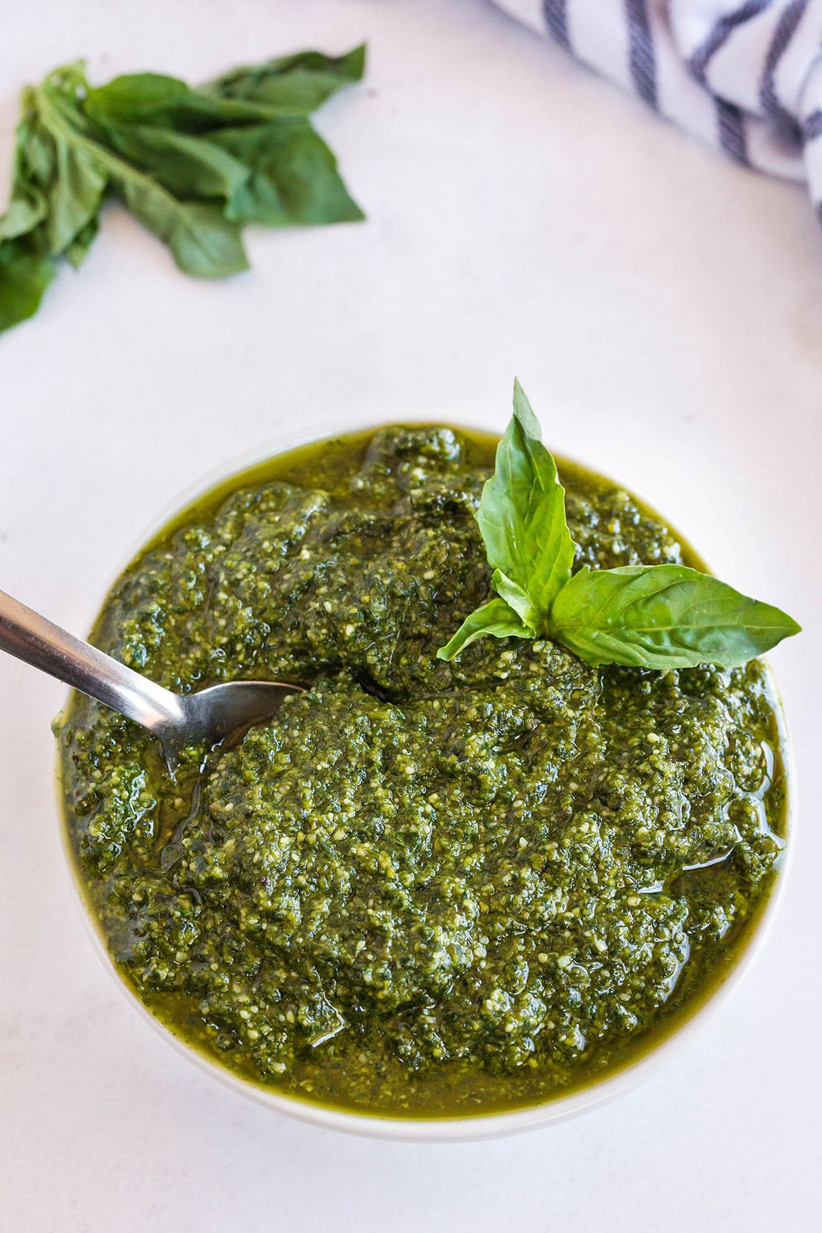Basil pesto sauce in a white bowl with a spoon and garnished with fresh basil.