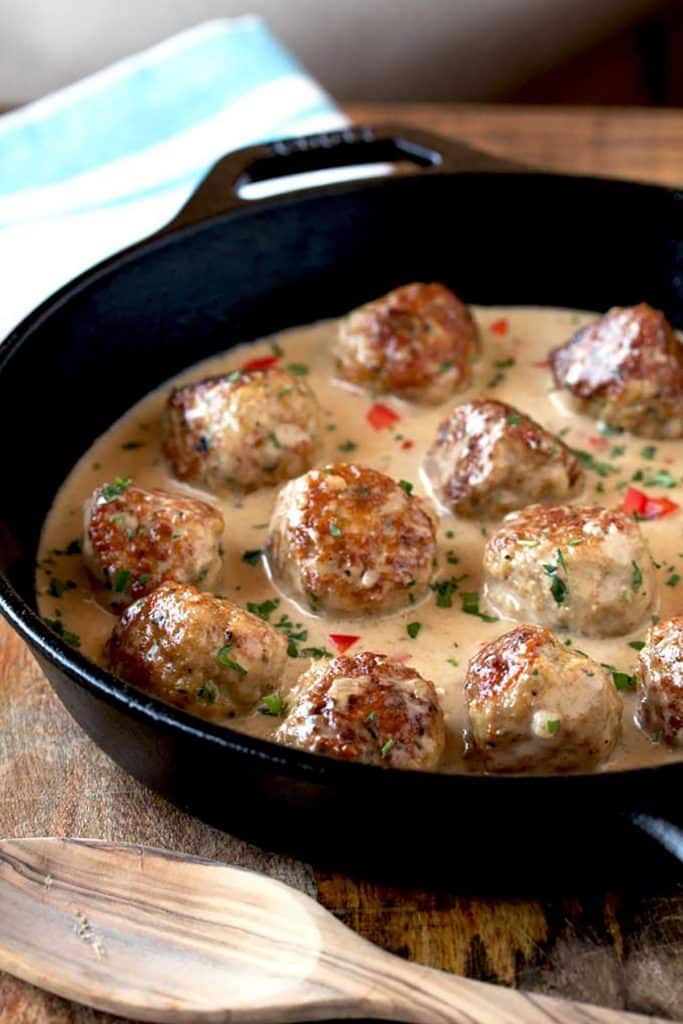 In this photo a cast iron skillet with Cajun Chicken meatballs in creamy sauce on a wooden table.