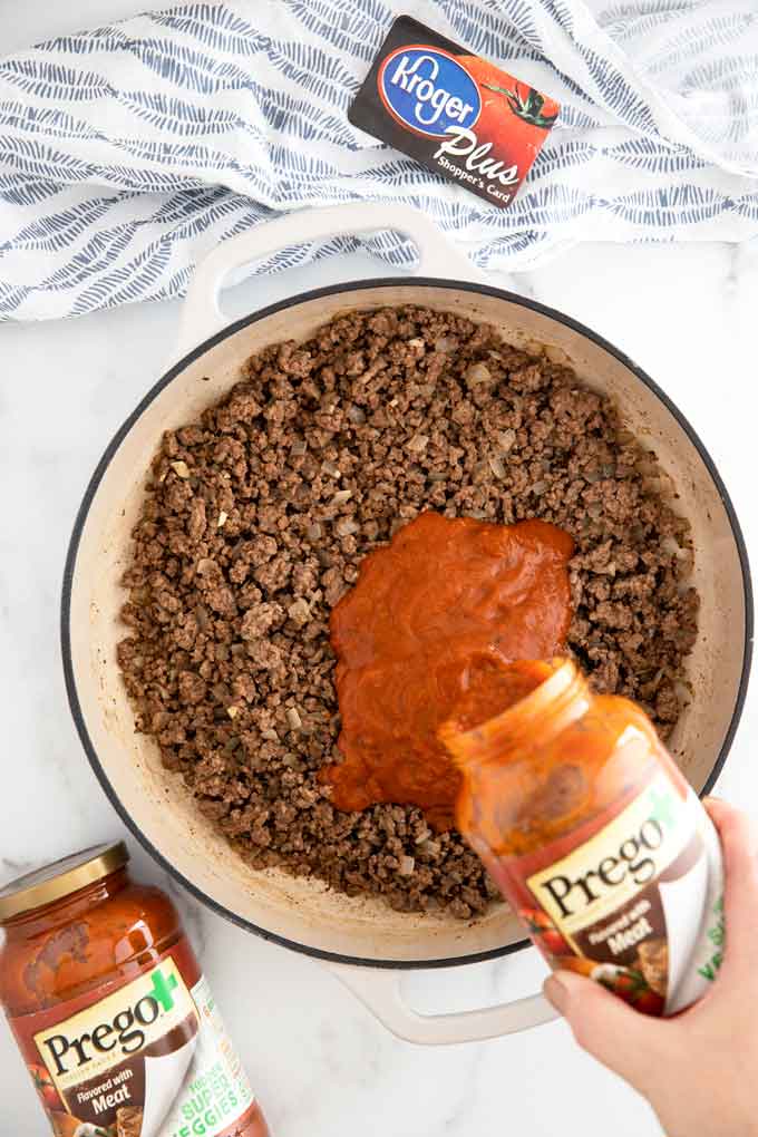 Prego pasta sauce being poured over browned ground beef.