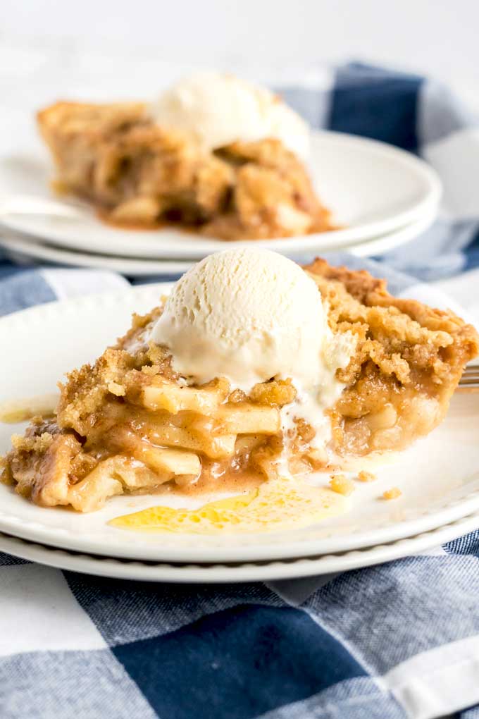 Sliced of apple pie with streusel crumb topping topped with vanilla ice cream on a white plate.