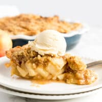 A slice of Crumble Apple Pie topped with vanilla ice cream on a white plate