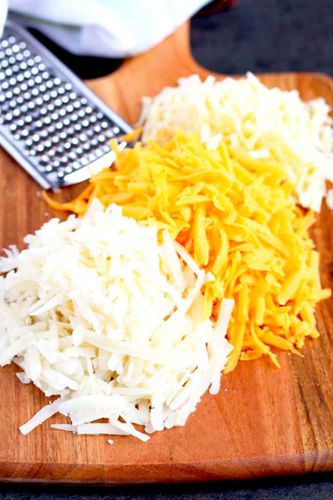 Three types of shredded cheese on a wooden board.