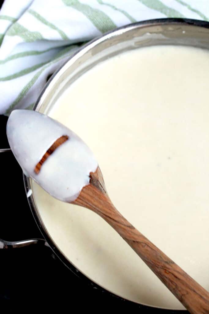 A saucepan with béchamel white sauce and a spoon showing the consistency of the sauce when is done.