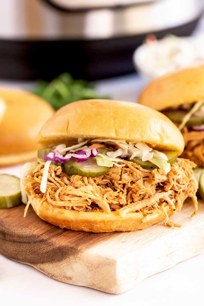 A BBQ pulled chicken sandwich with pickles and coleslaw on a wooden board.