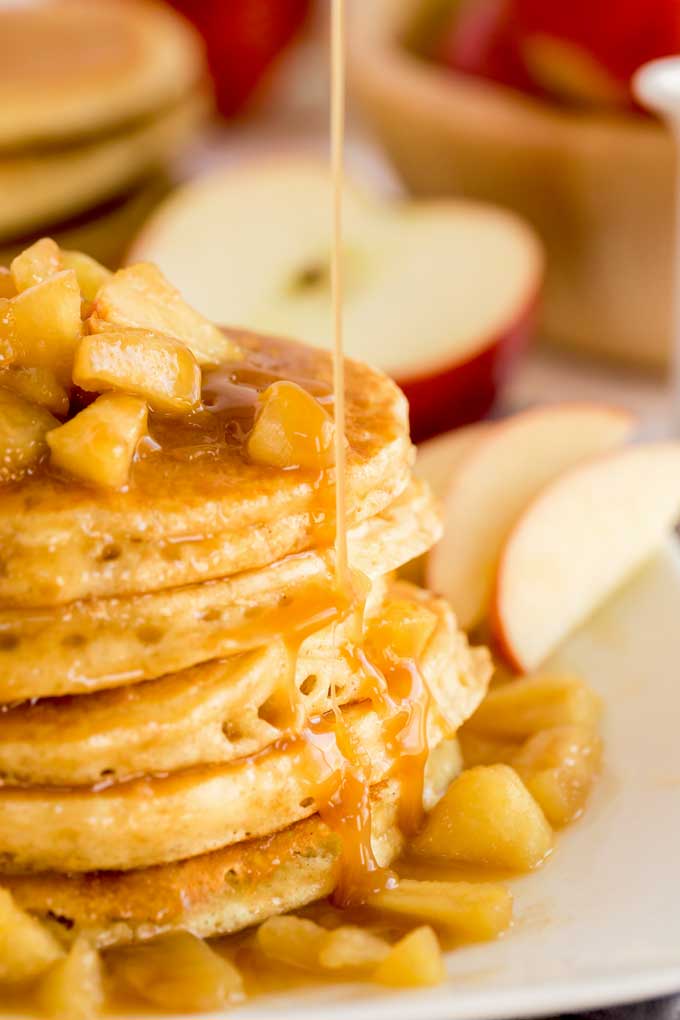 A stack of apple pancakes topped with caramel apples and drizzled with sweet caramel on a white plate