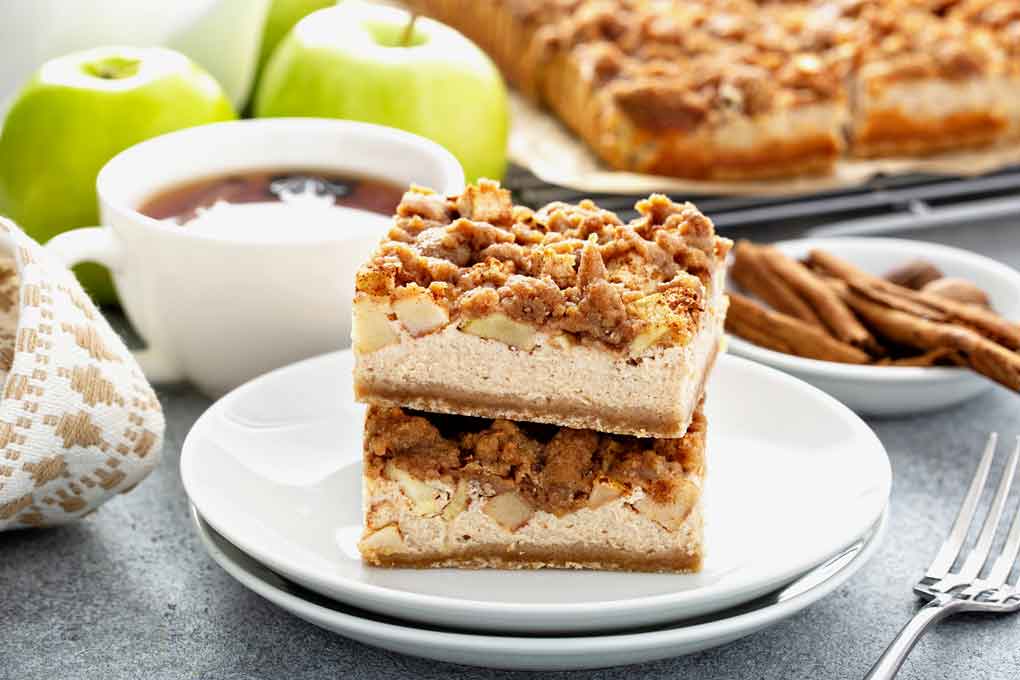 One apple cheesecake bars stacked on top of another on a white plate.