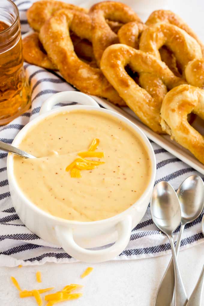 Warm pub-style cheese dip in a white bowl served with pretzels