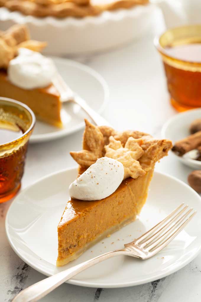 Slice of pumpkin pie topped with maple whipped cream on a white plate.