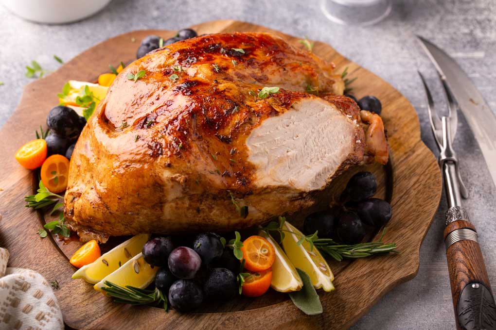 roasted turkey breast with a small side carved decorated with grapes and lemon slices.
