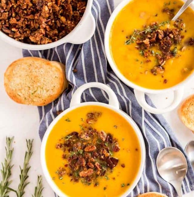 Bowls of butternut squash soup with pecan abcon topping on a white marble surface.