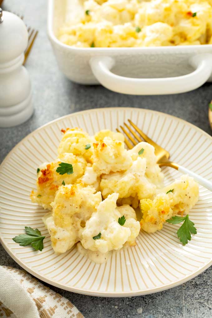 A serving of cheesy baked cauliflower au gratin on an ivory plate.