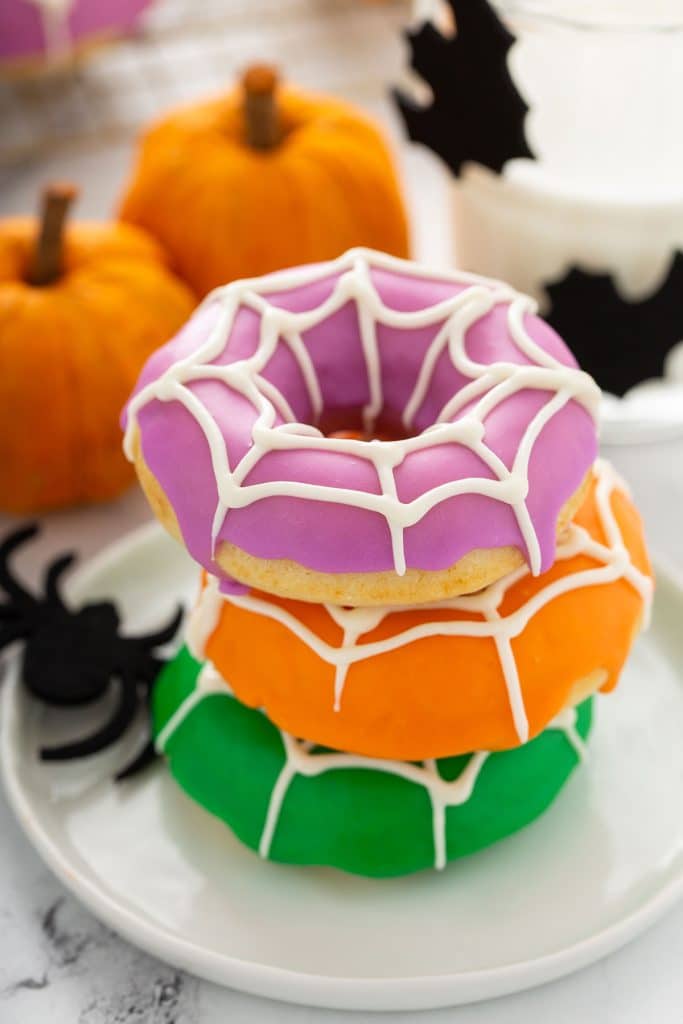 A trio of baked donuts glazed in Halloween colors with white chocolate cobwebs.