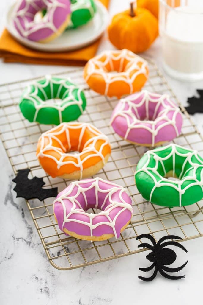 Colorful donuts with a web pattern piped on top sitting on a cooling rack.