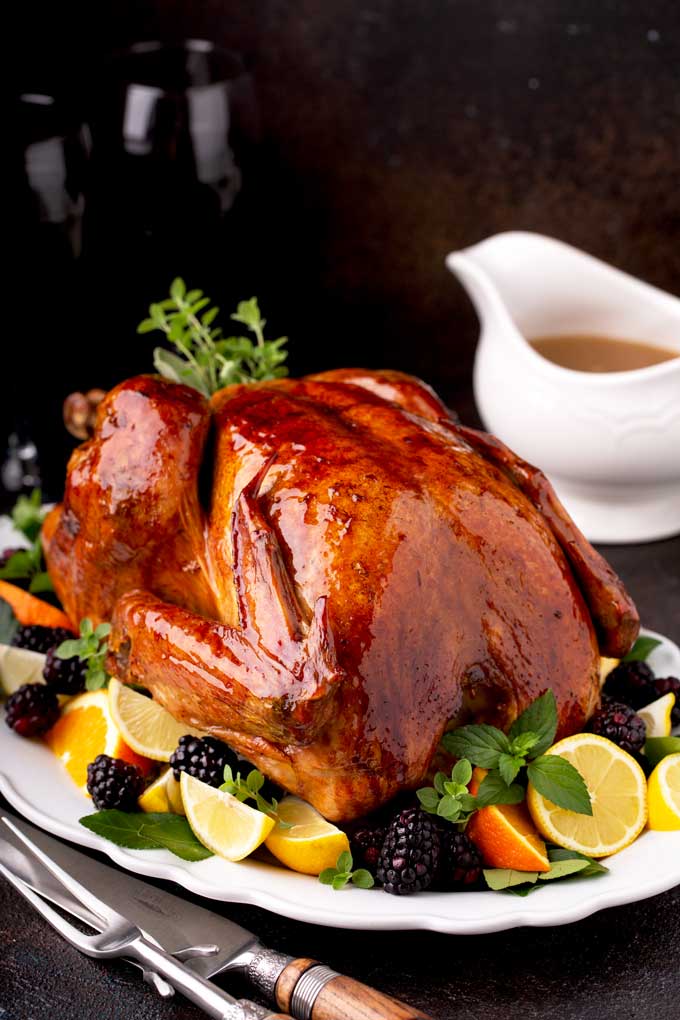 Whole roast turkey on a white platter garnished with herbs, fruits and citrus