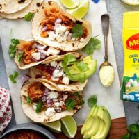 Tacos of chicken tinga with toppings on a white board