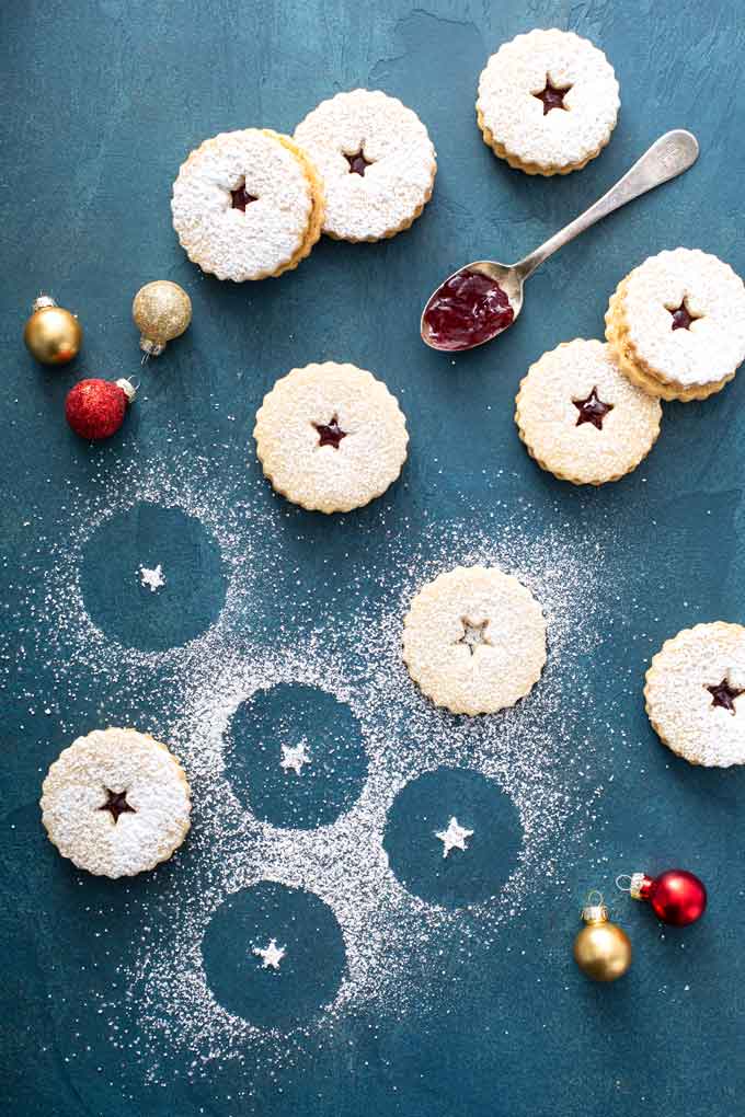 linzer cookies over a blue surface with confectioners' sugar all over.