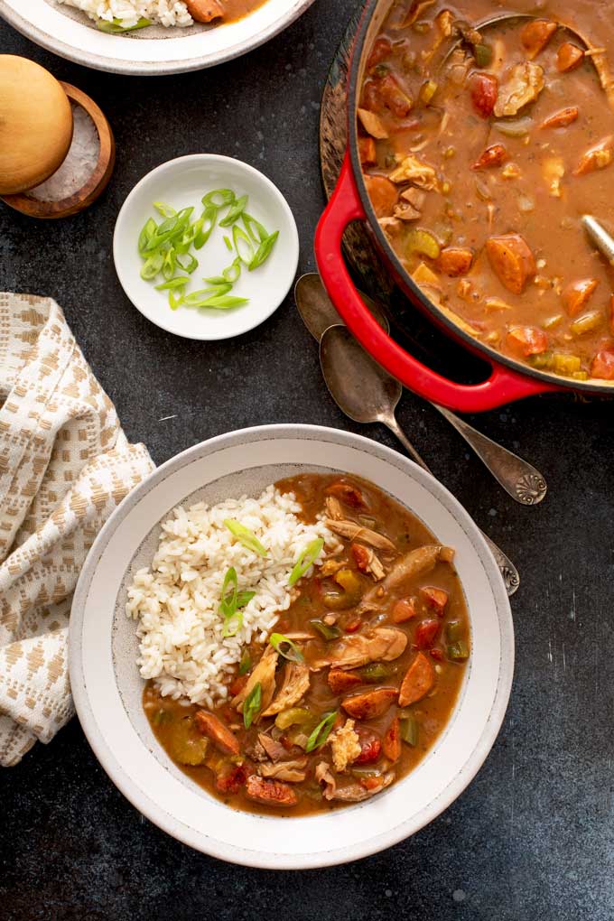 A serving of gumbo in a bowl with rice next to a Dutch oven