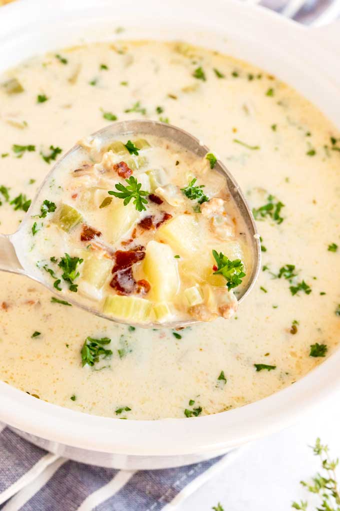 A ladle full with creamy clam chowder and topped with crispy bacon