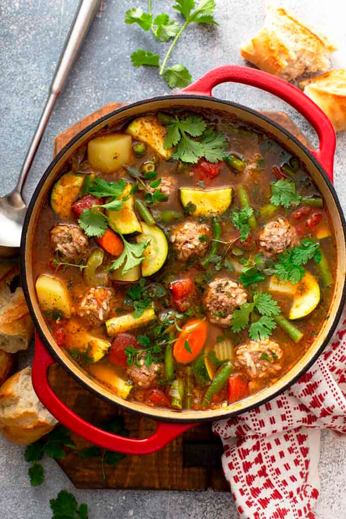 A big red pot of Albondigas Soup garnished with cilantro