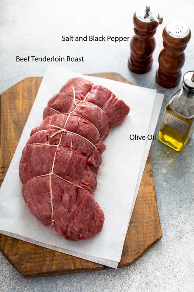 A trimmed and tied raw piece of beef tenderloin next to olive oil, salt and pepper.