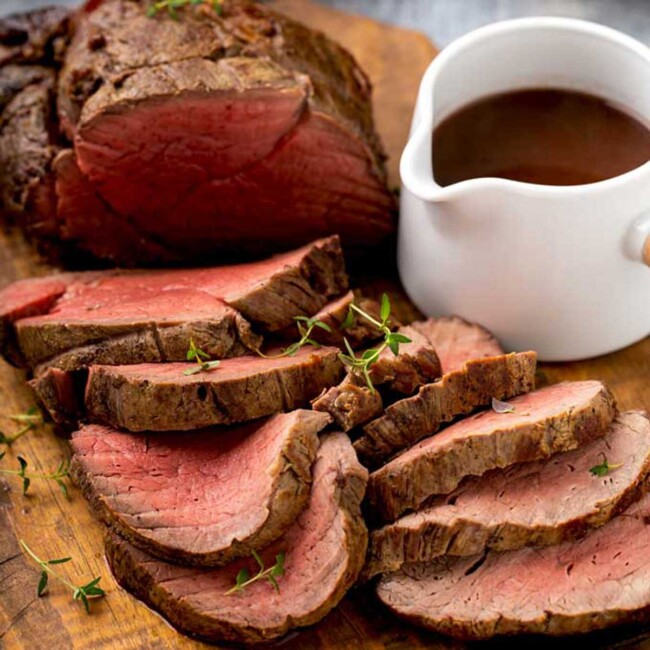 Beef tenderloin sliced next to a small pitcher with wine sauce