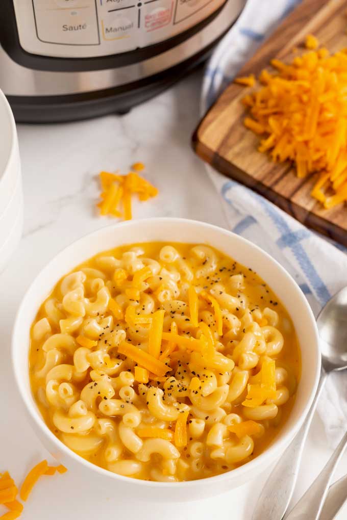 A bowl of mac and cheese next to a pressure cooker.